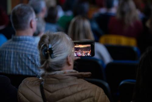 Zdjęcie przedstawia widza nagrywającego fragmet koncertu telefonem,.